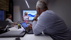 A diverse business coworkers actively participate in a corporate meeting. A female presenter shares crucial data analysis on a large screen, fostering collaborative discussion and strategic planning. - Powered by Shutterstock - Get 15% off with code: PIKWIZARD15