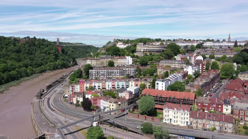 Aerial shot tracking past Hotwells and Clifton neighbourhoods with Clifton Suspension Bridge in the background in Bristol, England on a sunny day