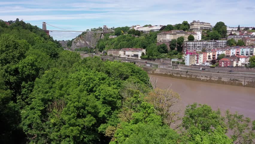 Aerial reveal over trees approaching Clifton Suspension Bridge, and the Avon River in Bristol, United Kingdom on a sunny day