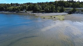 A coastal landscape is characterized by shallow waters where small waves break, rocks and houses along the shore, or a concrete tunnel carrying a stream dotted with algae. Metis-sur-mer, Quebec. - Powered by Shutterstock - Get 15% off with code: PIKWIZARD15