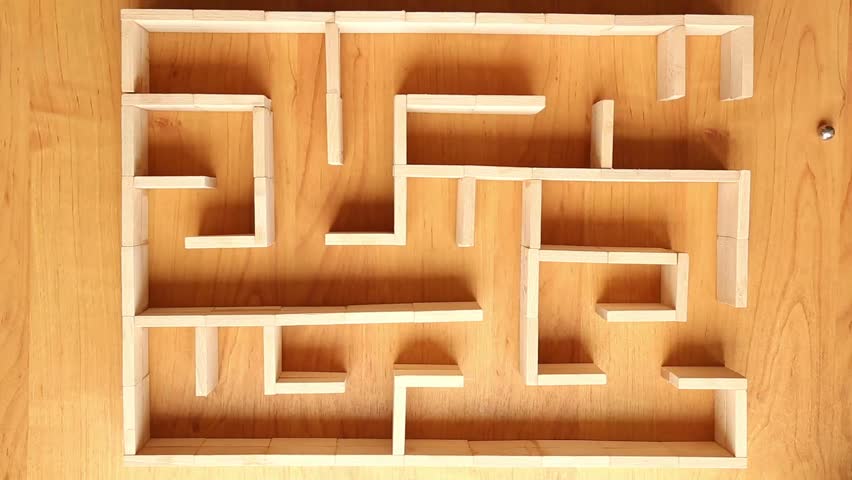 A small ball moves through a wooden labyrinth on a light surface, changing direction, demonstrating a steady forward movement.