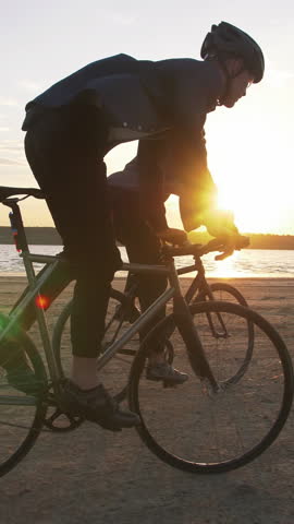 Two young men riding bicycles on the beach on the background of an orange sunsetting sky