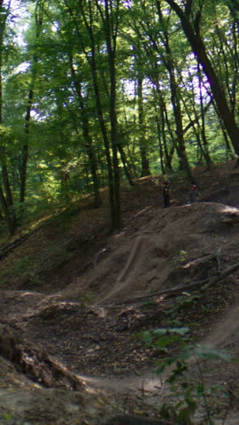 Male bicyclist exercises in dirt jumping rotating bike in air on forest hills slow motion. Extreme sportsman shows dangerous tricks in sunny country woods