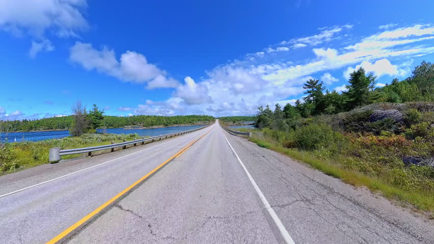 Scenic driving on Highway 6. Rocky nature mountain landscape forward road driving plate. Green forest and Canadian Shield in summer. Driving car POV front on asphalt road, Manitoulin Island, Ontario.