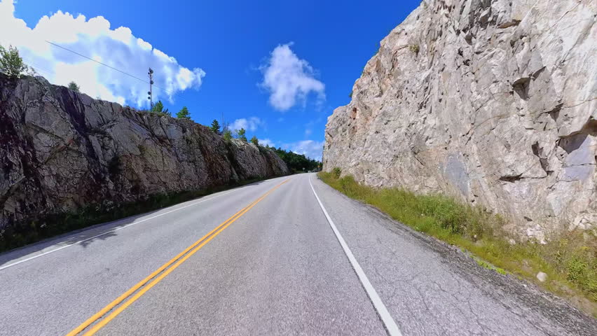 Scenic driving on Highway 6. Rocky nature mountain landscape forward road driving plate. Green forest and Canadian Shield in summer. Driving car POV front on asphalt road, Manitoulin Island, Ontario.