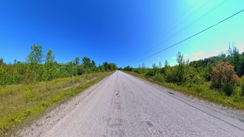 Straight country road back view driving plate POV, high side walls of lush trees. Driving car in country road at early fall in Manitoulin Island. Gibraltar Road near Lake Manitou, Ontario, Canada.