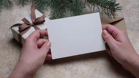 Hands present a blank greeting card above a wrapped Christmas gift, surrounded by pine branches, emphasizing the joy of giving and the holiday spirit, camera zooms in - Powered by Shutterstock - Get 15% off with code: PIKWIZARD15