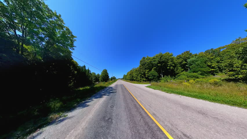 Straight country road back view driving plate POV, high side walls of lush trees. Driving car in country road at early fall in Manitoulin Island. Gibraltar Road near Lake Manitou, Ontario, Canada.