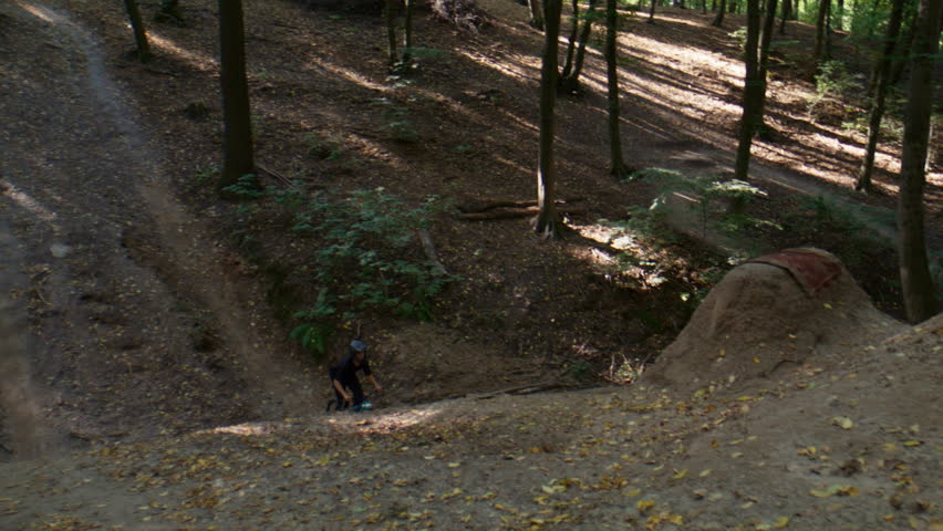 Young bicyclist shows dangerous superman seat grab on bicycle over hills in forest slow motion. Skilled athlete fails MTB bike landing after trick in park