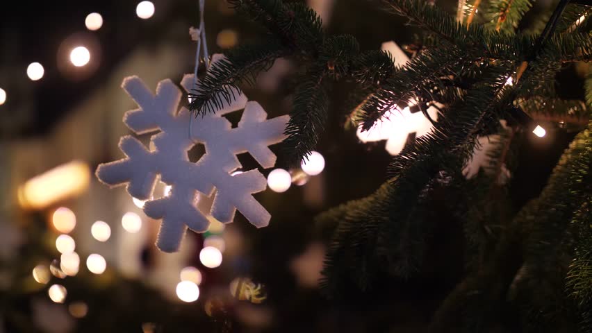 Xmas bokeh mood: white snowflake shaped Christmas ornament hanging outdoors in the illuminated Advent market at a Christmas market