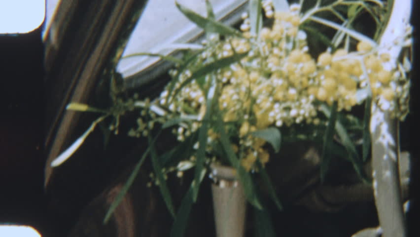 Vintage 8mm film showing a retro car interior with a small vase of flowers by the steering wheel, evoking classic charm and nostalgic detail