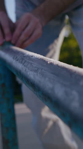 Hands of anonymous human placing sandpaper on railing with shabby paint and using force for better impact. Experienced freestyler polishing surface for ability of practicing better trick with sliding.