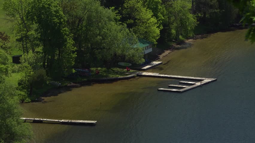 Wooden docks on a lake with a boathouse and recreational boats on the shoreline during a hot summer day.