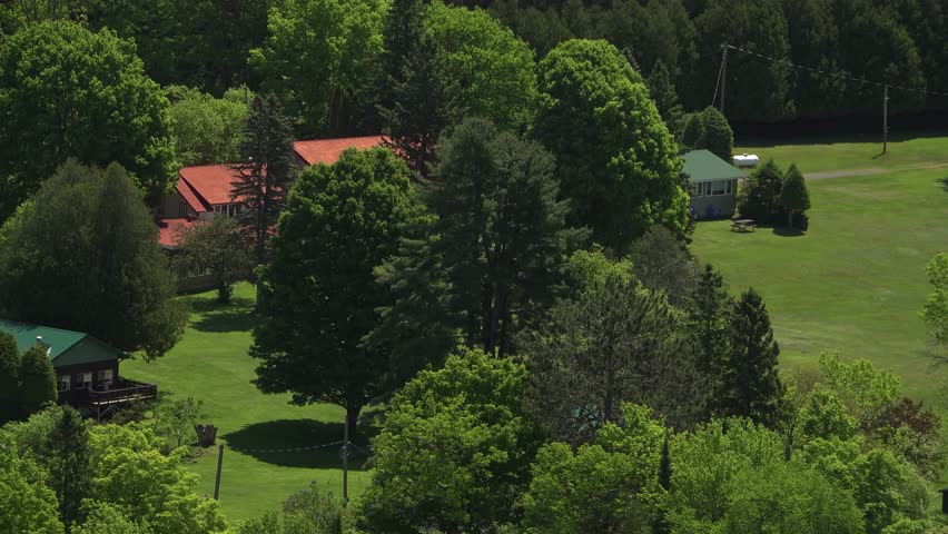 Zooming out on cabins and docks on a lake surrounded by forest in cottage country during the summer.