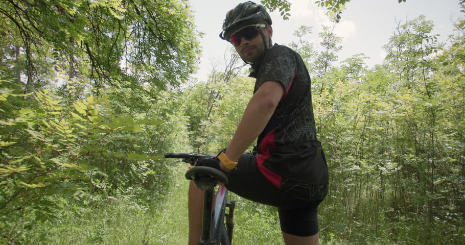 A man riding a bike through a lush green forest. Mountain biker in nature. Back view. Recorded at 120 fps on cinema camera.