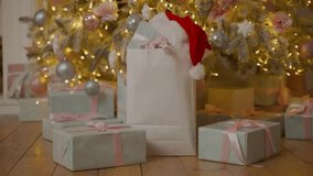 A detailed 4K view of gifts and decorations under a Christmas tree featuring a Santa hat in a white bag and pink ornaments. - Powered by Shutterstock - Get 15% off with code: PIKWIZARD15