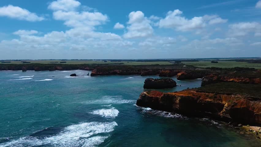 Witness the dramatic fusion of turquoise ocean and fiery orange cliffs along the Great Ocean Road. Colossal sea stacks stand sentinel in Victoria, Australia.