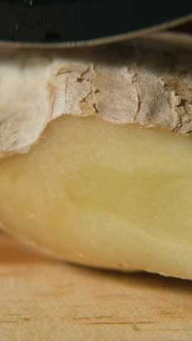 Vertical video. Macro closeup of cutting fresh ginger root on wooden surface, showing fibrous texture and freshness, natural detox and healthy lifestyle concept
