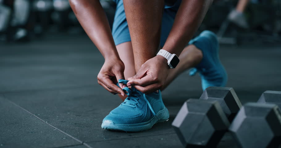 Person, hands and tying with shoes in gym for fitness, workout preparation or start exercise. Closeup, active or getting ready with tie, sneaker or laces for indoor training or run in health club