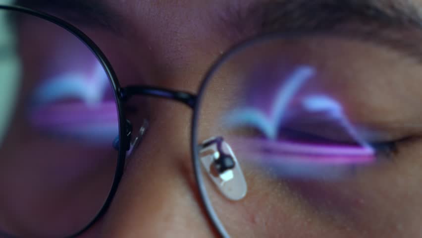 A person wearing glasses works on a laptop, with a glowing digital open book reflected in the lens. Highlights e-learning, digital reading, online education, knowledge access, and modern technology.

