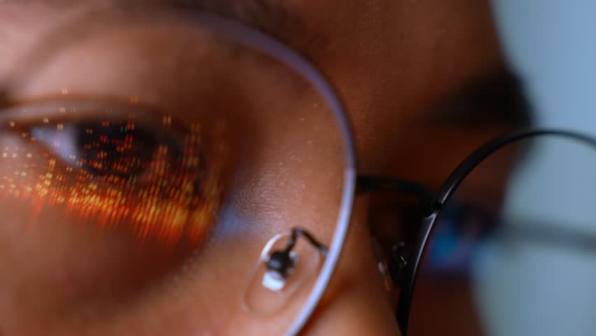 A person wearing glasses uses a laptop as real-time digital data graphs reflect on the lenses, symbolizing analytics, performance tracking, fintech, decision-making, and digital intelligence.

