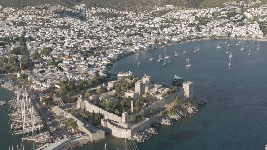D-Log M. Bodrum, Turkey. Aerial drone shot of coastal Bodrum Castle fortress with yachts moored in front, beaches and white houses along shore. Aerial View, MasterShots, Spiral forward