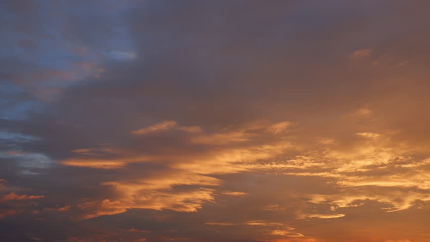 A dramatic sunset sky timelapse featuring fiery altostratus and stratocumulus clouds glowing in deep orange and gold, creating a dynamic, textured scene across the evening horizon. Time-lapse.
