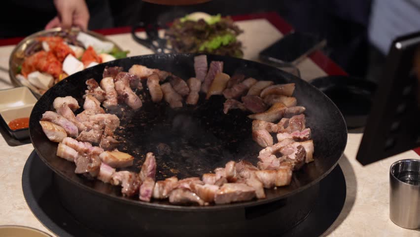 Authentic Korean Food Experience, Adding Kimchi and Vegetables to Sizzling Pork Belly on Korean BBQ Griddle, Cooking Pork and Spicy Kimchi Together on Hot Plate