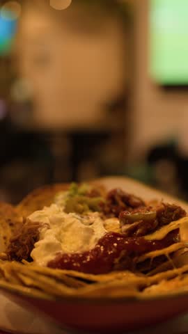 Close-up of nachos with salsa, sour cream, cheese, and hand reaching in warm indoor lighting