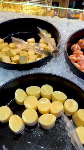 Various tofu, fish cakes, shrimp balls, and noodles arranged on ice under bright buffet lighting