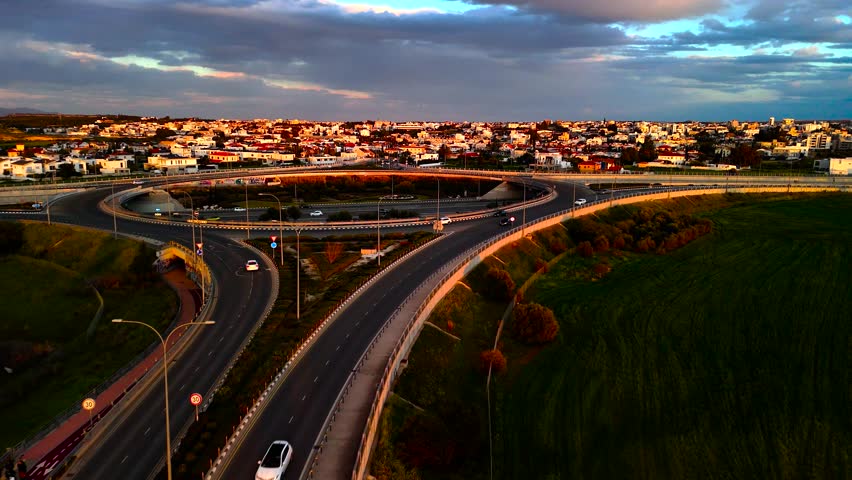 A stunning view of a winding road at sunset, surrounded by fields and a peaceful town. The warm light reflects off the landscapes, creating a serene atmosphere.