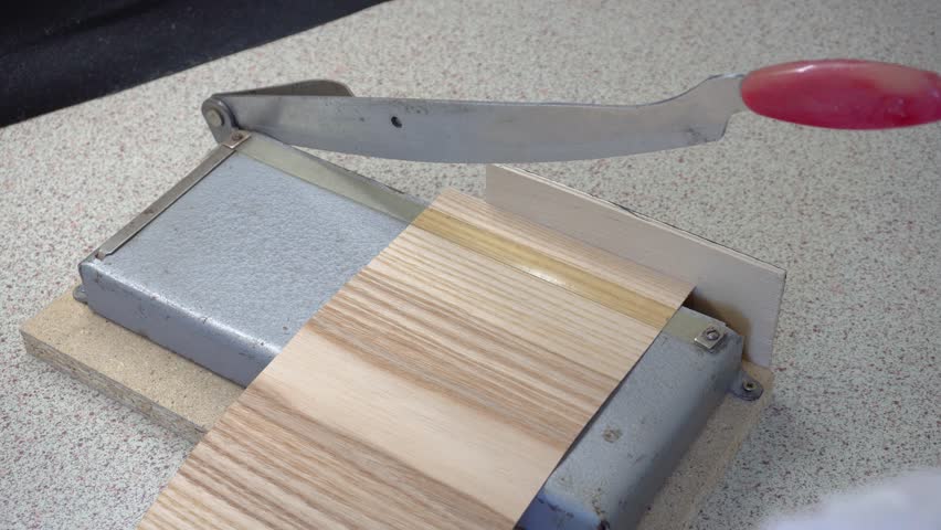 A hand veneer cutter is used to cut thin strips of wood for candle wicks. Manual cutting of veneer sheets.