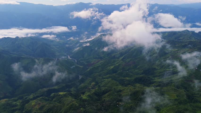 Aerial drone view of majestic green mountain ranges and deep valleys covered in low-lying clouds and mist. Scenic highland landscape in Davao Philippines showing the vast tropical wilderness.