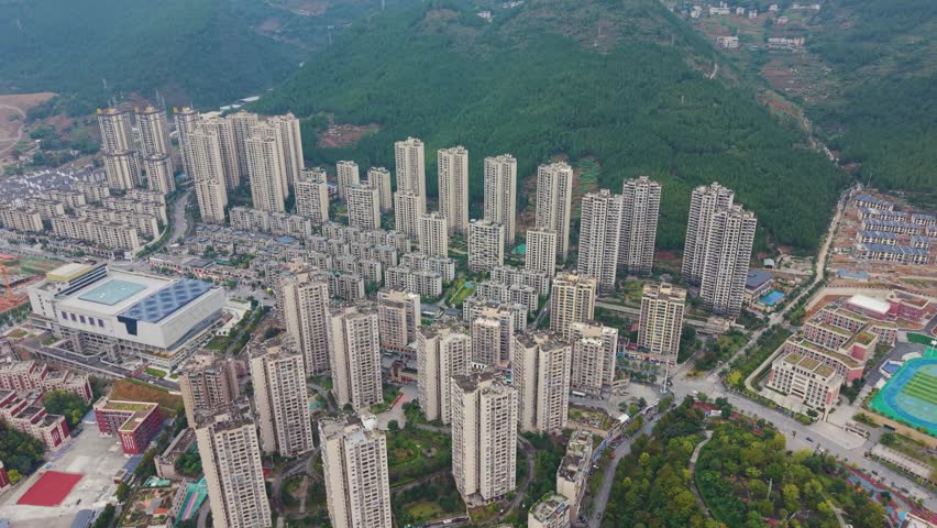 Aerial of Wuxi’s modern skyline with dense high rises set against a lush mountain backdrop, urban growth and scenic contrast ideal for travel, architecture, and cityscape projects. China, UHD.