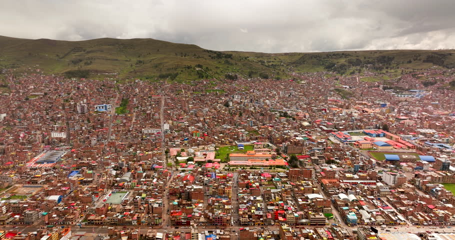 Wide aerial view, Puno, Peru, revealing dense urban streets and hillside neighbourhoods near Lake Titicaca, captured under overcast skies in the Andean highlands