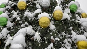 Happy New Year and Merry Christmas. Video of snow-covered city Christmas tree decorated with glass green and yellow balls at cold winter snowy day. New Year festive background. Close-up view - Powered by Shutterstock - Get 15% off with code: PIKWIZARD15