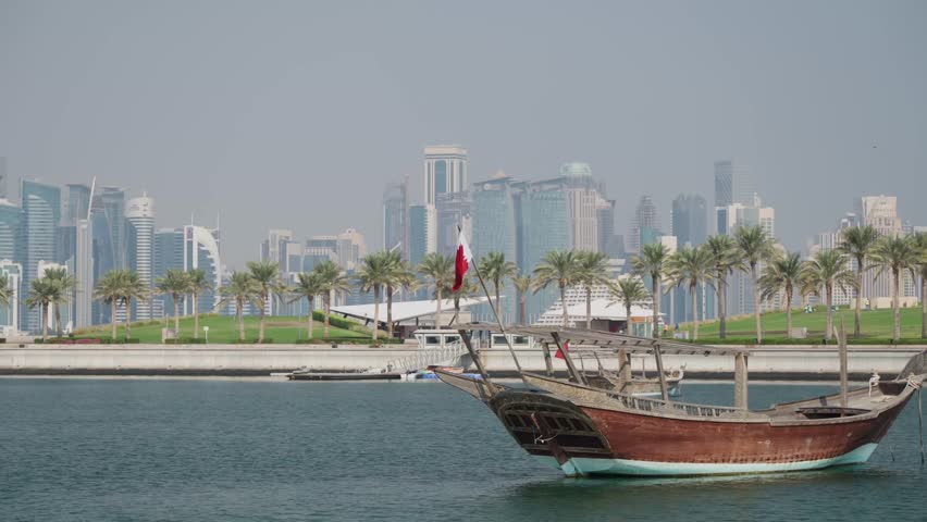 Boat with Qatar flag swinging in doha city marina and skycrapers skyline