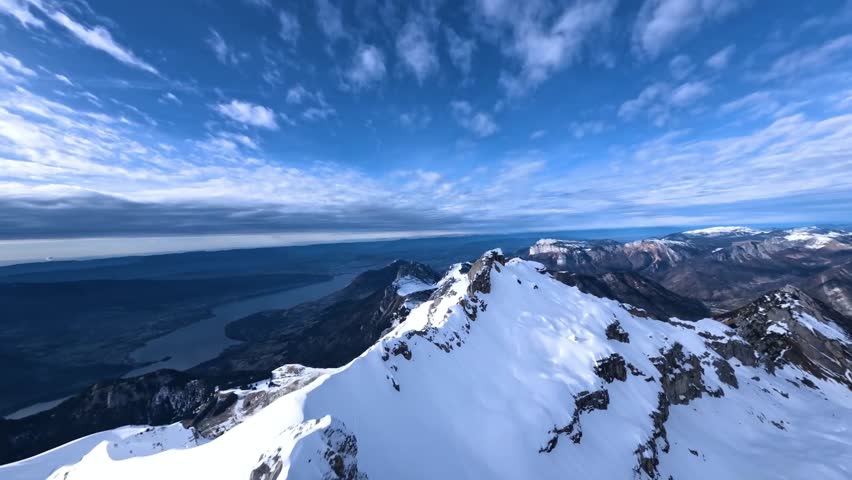 Majestic FPV drone footage flying over a vast, untouched snowfield on a mountain peak. The flight reveals a stunning panoramic view of the entire snow-capped Alps mountain range in the distance.