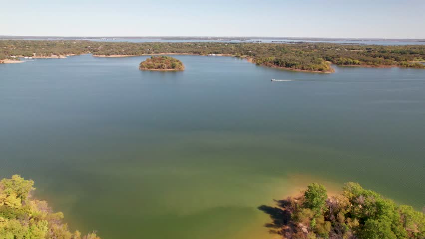 Aerial flight over Lake Lewisville towards an island. A boater is seen heading approximately west in front of the island.