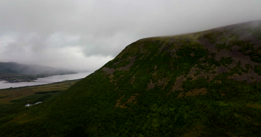 Aerial view of a misty green mountain above Sortland in Northern Norway, with low clouds, fjords and dramatic coastal landscape in Vesterålen during a calm, moody day