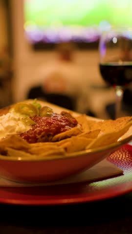Tortilla chips with salsa and sour cream in warm sports bar lighting, shallow focus.