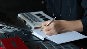 Music producer writing music composition notes in a notebook at a home studio desk with a laptop and MIDI keyboard controller, red usb interface, planning new beats and sound sequences during daylight - Powered by Shutterstock - Get 15% off with code: PIKWIZARD15