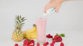 Hand tops pink smoothie with whipped cream, surrounded by pineapple, banana, strawberries, raspberries, bright lighting - Powered by Shutterstock - Get 15% off with code: PIKWIZARD15