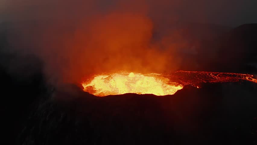 Aerial view of active volcano crater overflowing with lava river at night. Glowing magma flowing out of vent with smoke.