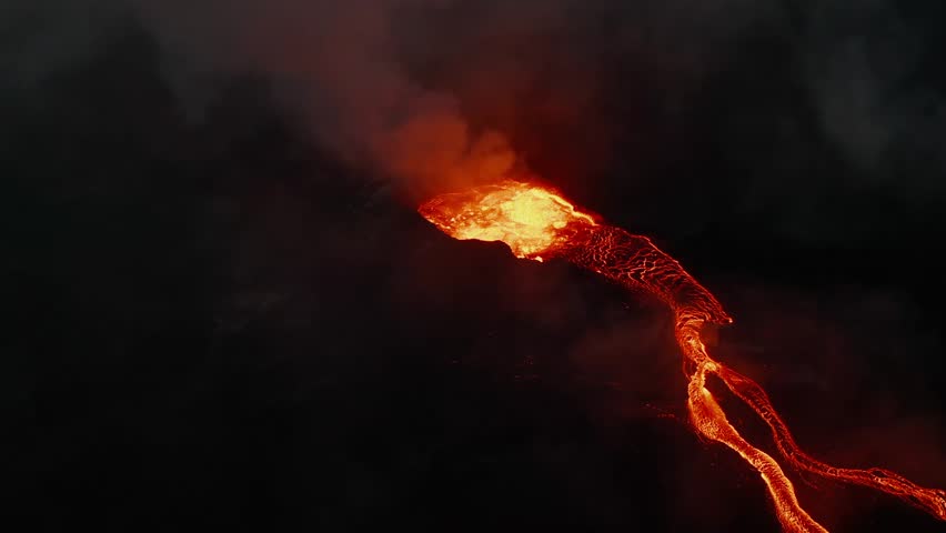 Aerial drone view of active volcano crater erupting lava and smoke at night. Glowing magma rivers flowing down from the vent.
