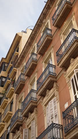 Low angle view of traditional residential buildings in Alicante, Spain, featuring ornate facades, wrought iron balconies, and shuttered windows. Vertical