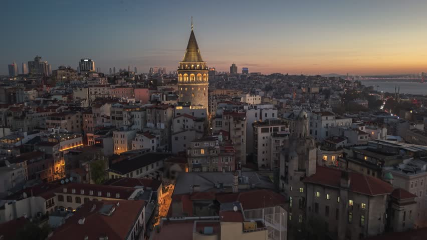 Morning view of Galata Tower and cityscape in Istanbul with lights illuminating streets and buildings at sunrise. Flying around iconic Galata Tower in historic Beyoglu district 