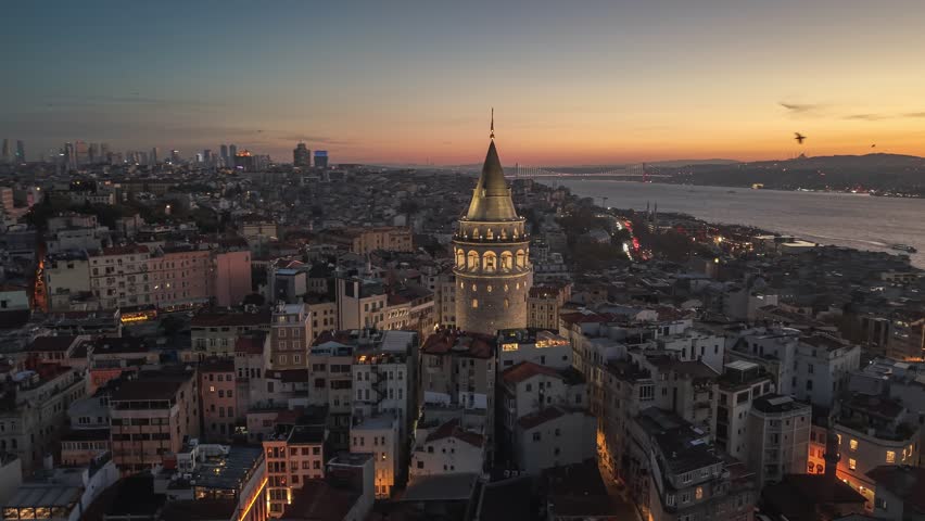 Morning view of Galata Tower and cityscape in Istanbul with lights illuminating streets and buildings at sunrise. Flying around iconic Galata Tower in historic Beyoglu district 