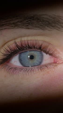 Vertical video of Woman opening her beautiful blue eyes, looking at the camera smiling, while the light illuminated her upper and midface area, close up shot. Duchenne smile concept.