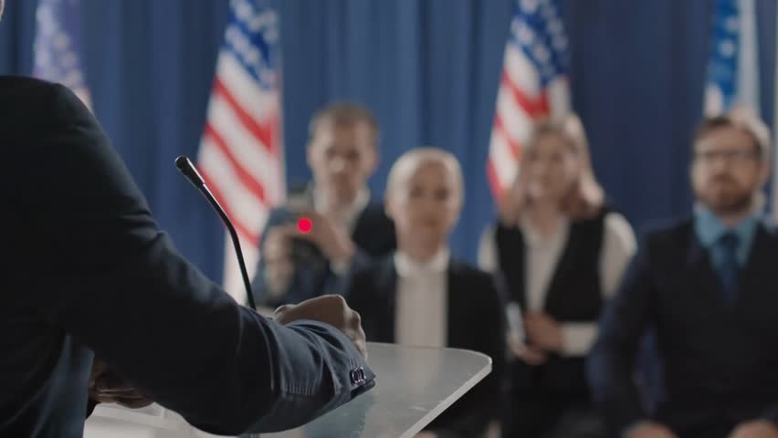 An unrecognizable African-American political candidate finishing a speech at a podium, addressing an audience during a formal campaign event.